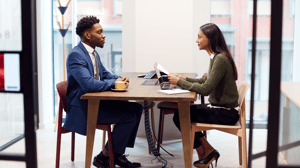 Woman asking a man who is seated across the table if he has any questions at the end of his interview.