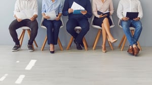 Five employers are sitting in a row and reading resumes as they wait for hiring help from Inova Staffing.