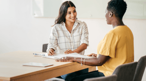 Two women sitting across from one another at a table, smiling and talking.